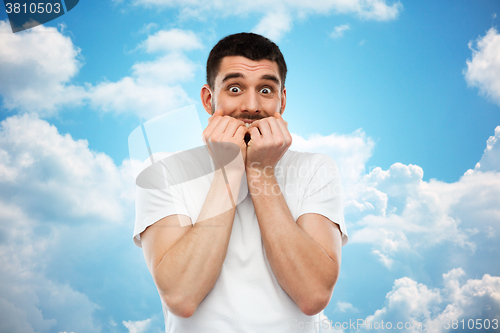 Image of scared man in t-shirt over blue sky background