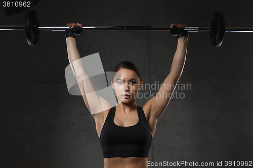 Image of young woman flexing muscles with barbell in gym