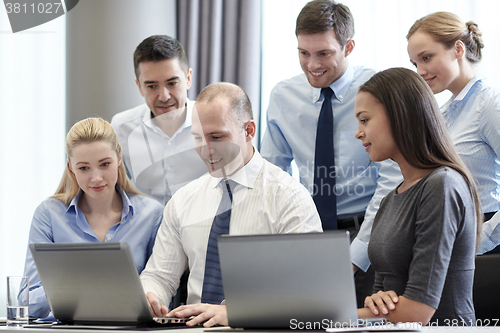 Image of smiling businesspeople with laptops in office