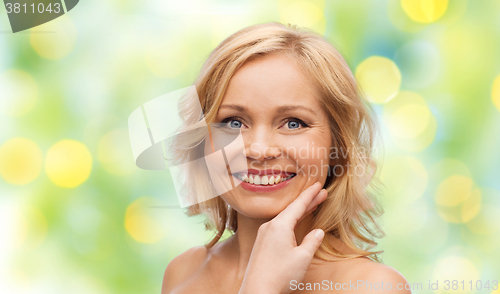 Image of smiling woman with bare shoulders touching face