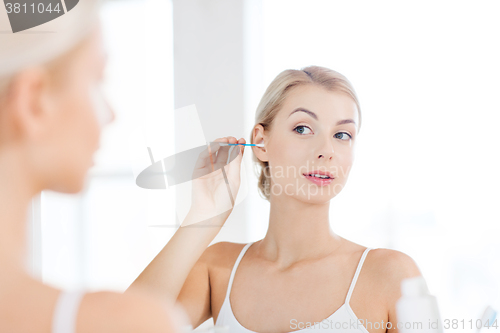 Image of woman cleaning ear with cotton swab at bathroom