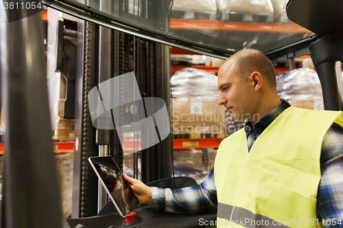 Image of man with tablet pc operating forklift at warehouse