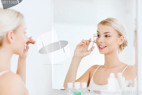 Image of woman with curler curling eyelashes at bathroom