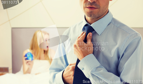 Image of close up of man adjusting tie on neck in bedroom