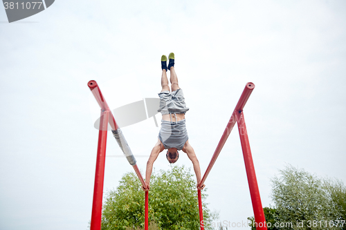 Image of young man exercising on parallel bars outdoors