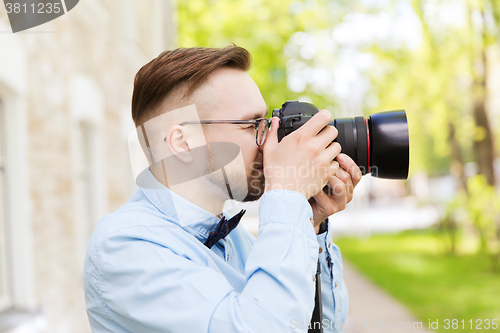 Image of young hipster man with digital camera in city