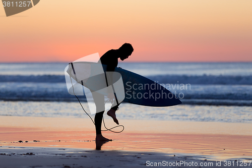 Image of Silhouette of surfer on beach with surfboard.