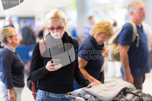 Image of Female traveler using cell phone while waiting on airport.