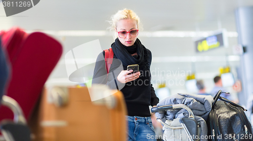 Image of Female traveler using cell phone while waiting on airport.