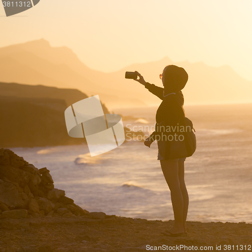 Image of Woman snaping photo of La Pared beach in sunset.