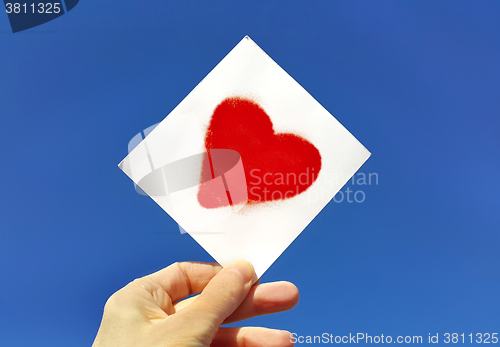 Image of Hand holding a picture of a heart against the blue sky