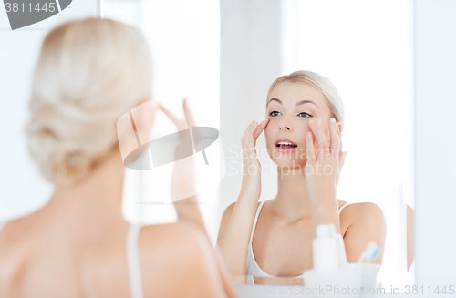 Image of happy woman applying cream to face at bathroom