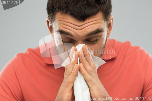 Image of sick man blowing nose to paper napkin at home