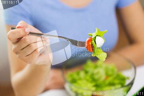 Image of close up of young woman eating salad at home