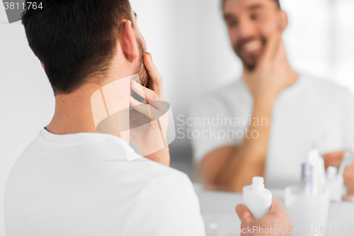 Image of close up of man applying cream to face at bathroom