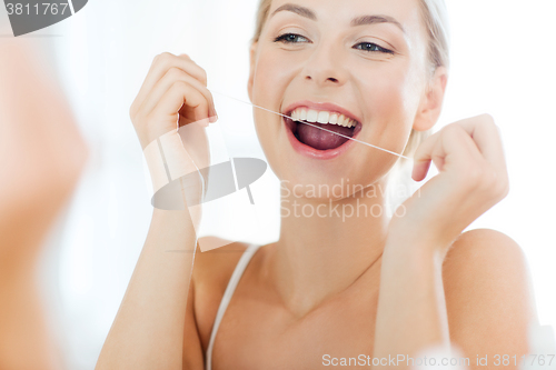 Image of woman with dental floss cleaning teeth at bathroom