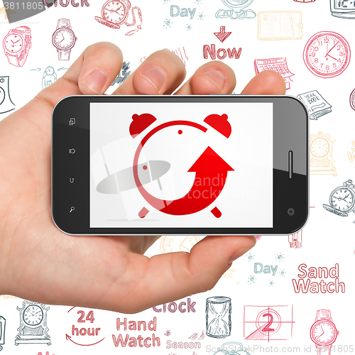 Image of Time concept: Hand Holding Smartphone with Alarm Clock on display