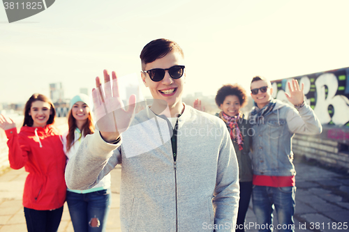 Image of happy teenage friends waving hands on city street