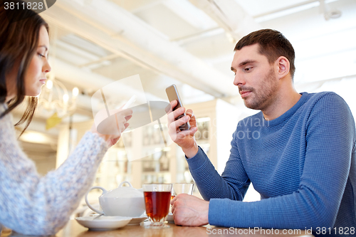Image of couple with smartphones drinking tea at cafe
