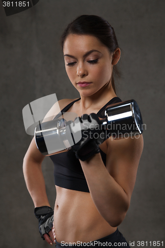 Image of young woman flexing muscles with dumbbells in gym