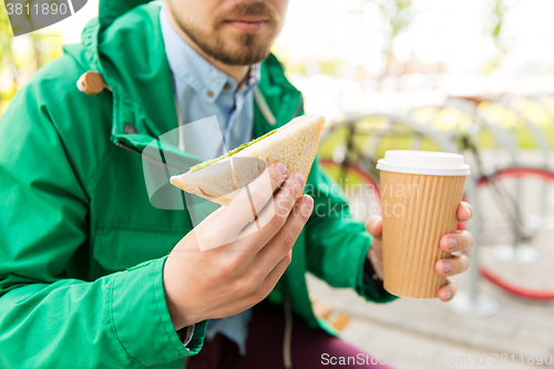 Image of close up of man with coffee and sandwich on street