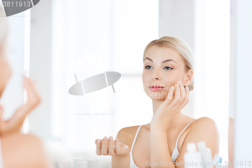 Image of happy woman applying cream to face at bathroom