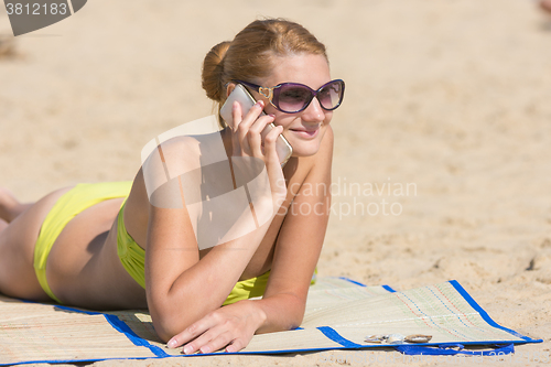 Image of Happy girl lying on the beach and talking on the phone