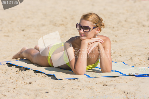 Image of The girl lies on a mat on the beach and looking to the left