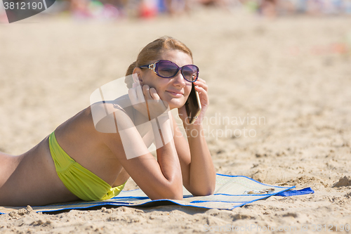 Image of Happy girl sunbathing on the beach and talking on the phone