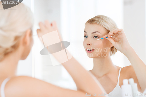 Image of woman fixing makeup with cotton swab at bathroom