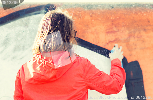 Image of woman drawing graffiti with spray paint from back