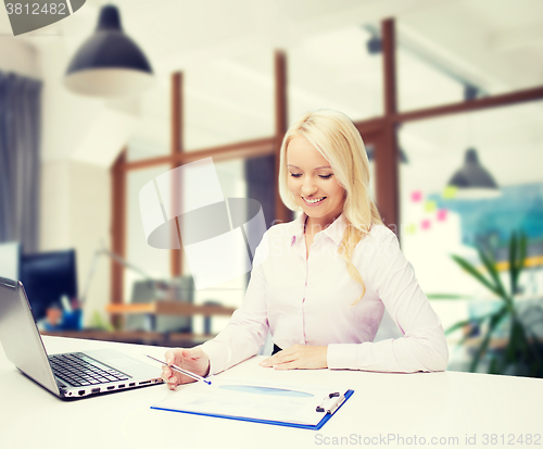Image of smiling businesswoman reading papers in office