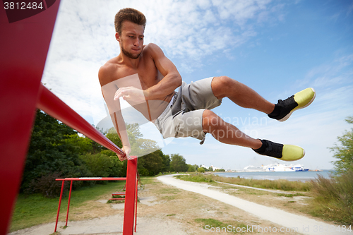 Image of young man exercising on horizontal bar outdoors