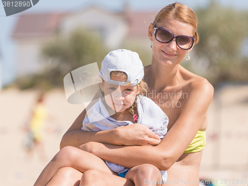 Image of Young mother warms her frozen daughter on the sandy banks of the river