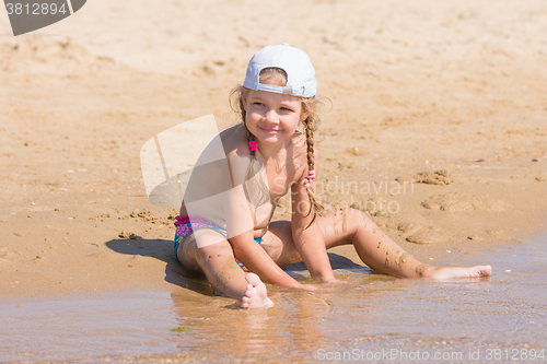 Image of Five-year girl in a cap sits on the sand on beach