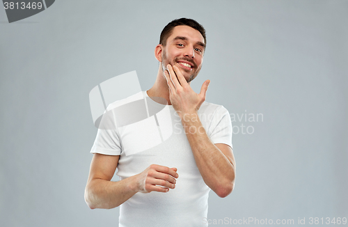 Image of happy young man applying cream or lotion to face