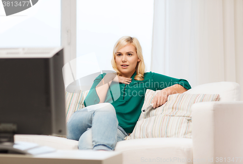 Image of smiling woman with remote watching tv at home