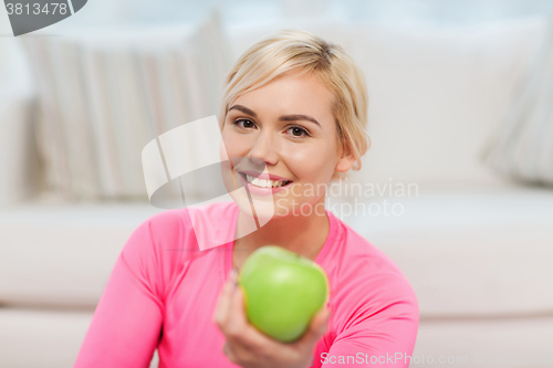 Image of happy woman eating green apple at home