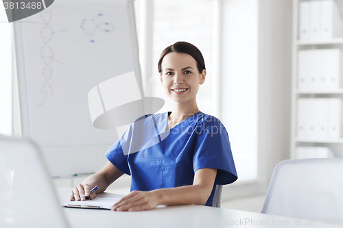 Image of happy female doctor or nurse writing to clipboard