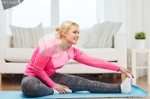 Image of happy woman stretching leg on mat at home