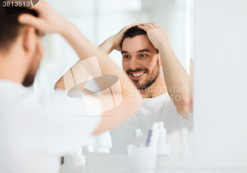 Image of happy young man looking to mirror at home bathroom