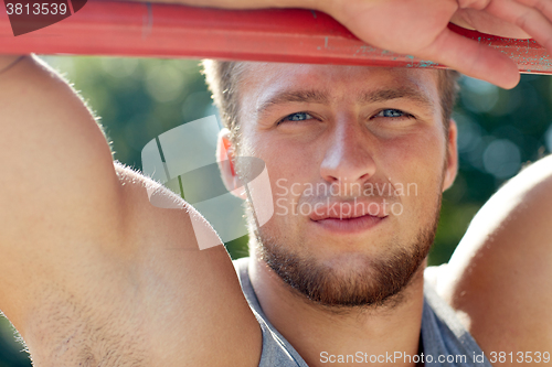 Image of young man exercising on horizontal bar outdoors