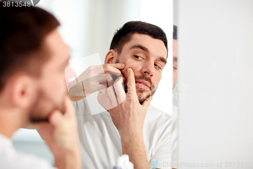 Image of man squeezing pimple at bathroom mirror