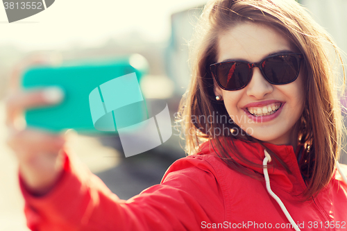 Image of smiling young woman taking selfie with smartphone