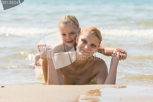 Image of Mum with a daughter on his back lying on the beach and smiling