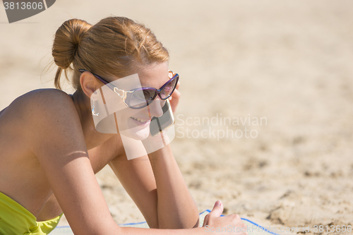 Image of Happy girl lying on the sandy beach talking on the phone