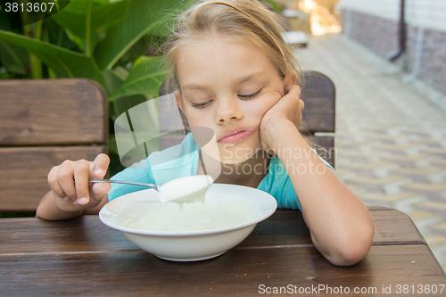 Image of Upset six year old girl looking sadly at the semolina in a spoon at breakfast