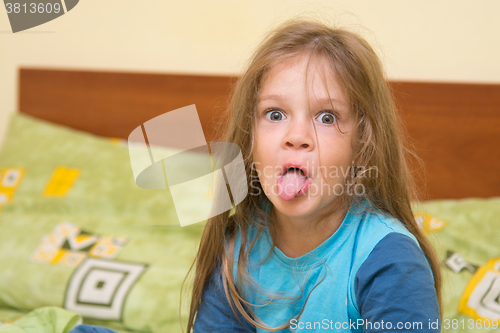 Image of Five-year girl waking up sitting on the bed and showing tongue