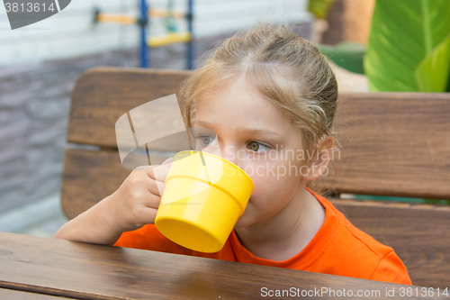 Image of Four-year-girl drinking a drink sitting at the table on the veranda