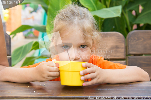 Image of Four-year girl drinks a drink from the cup and looks in the frame